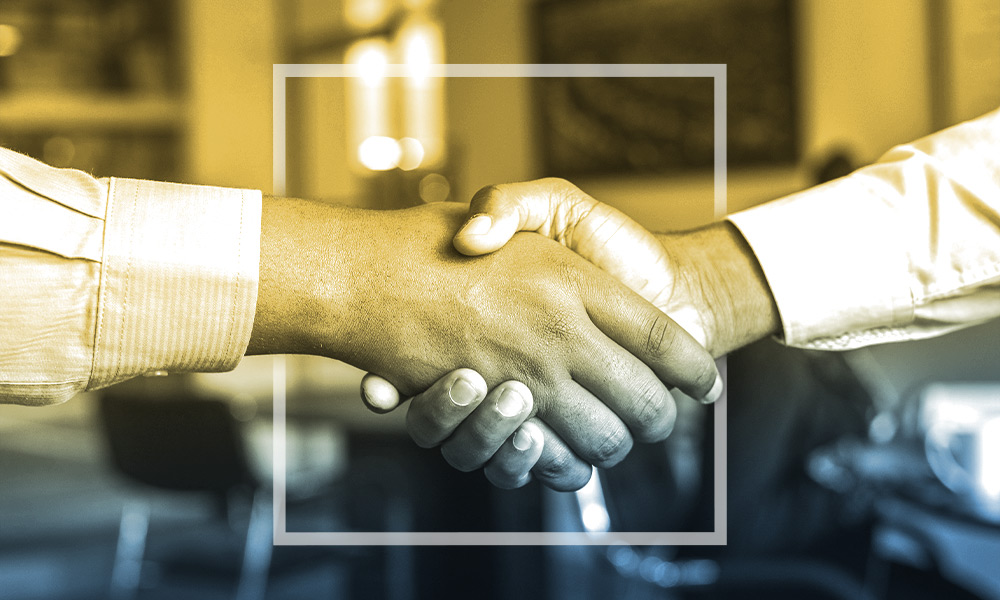 Two people of color shaking hands wearing dress shirts.