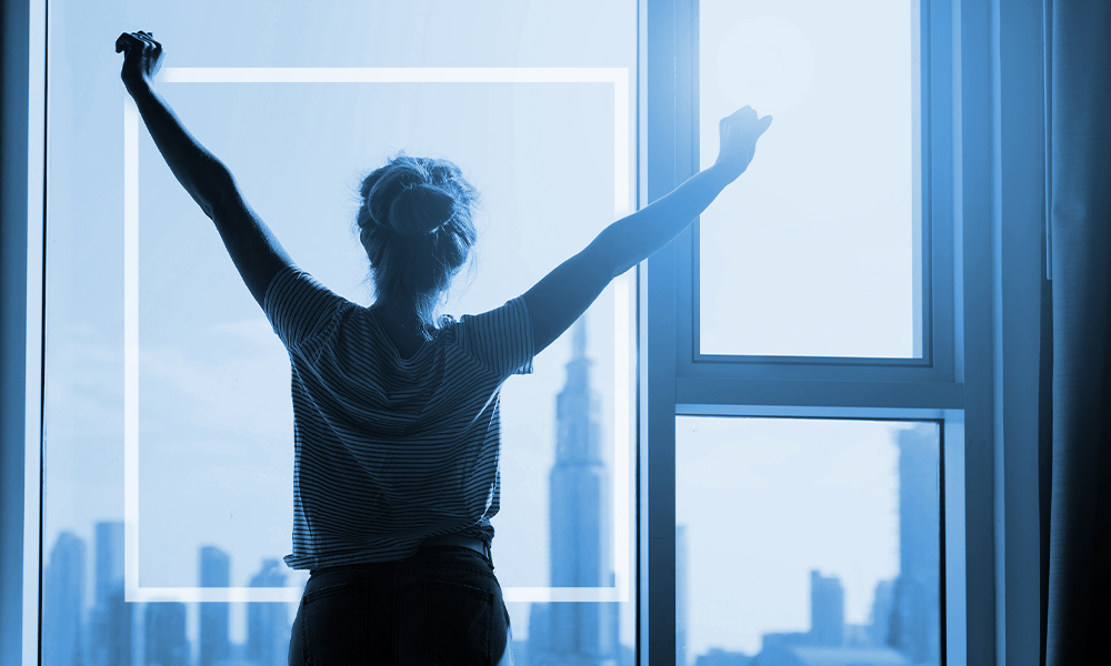 Woman stretching after waking up and checking out the view from her window.