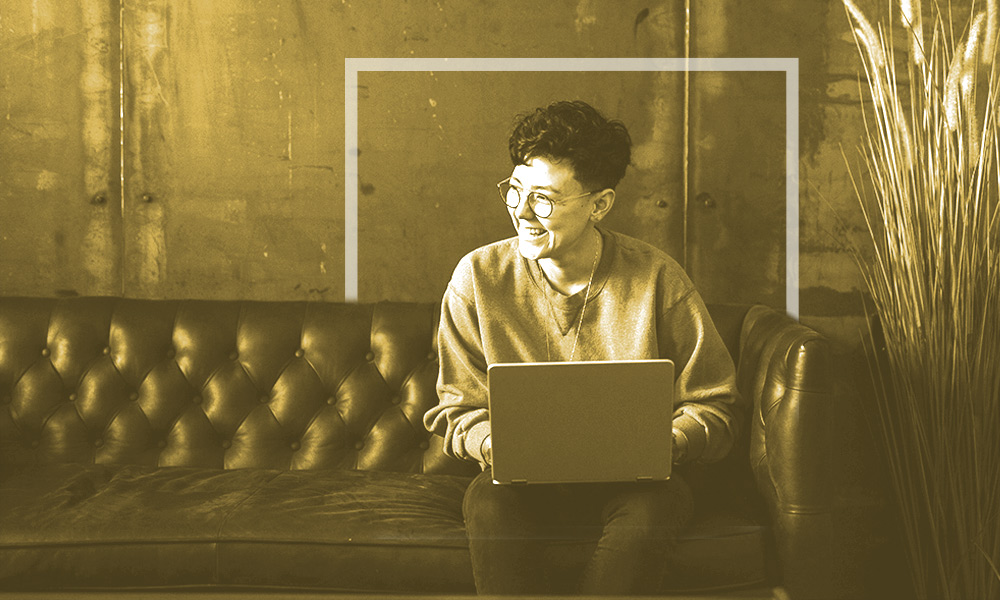 Women with glasses and big smile clearly enjoying herself and conversing with someone while on computer.