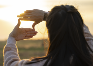 Woman framing sunset with hands on beach